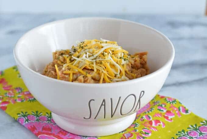 Refried beans topped with shredded cheese in a bowl.