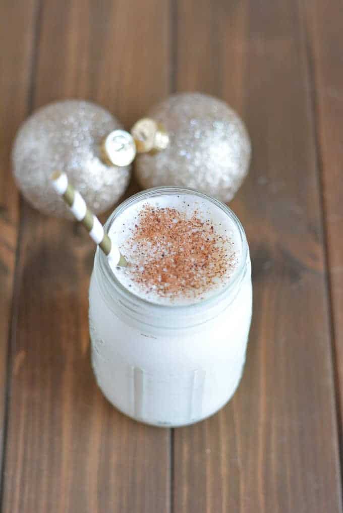 Eggnog Protein Shake on a brown wood table next to gold Christmas balls.