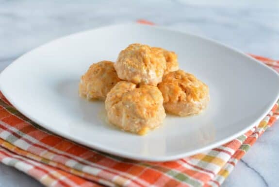 Ground chicken meat balls with buffalo sauce on a white plate.